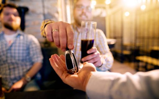 Drunk man with a beer in hand giving car key to the sober friend while enjoying in the bar. Close up focus view of key and hands.